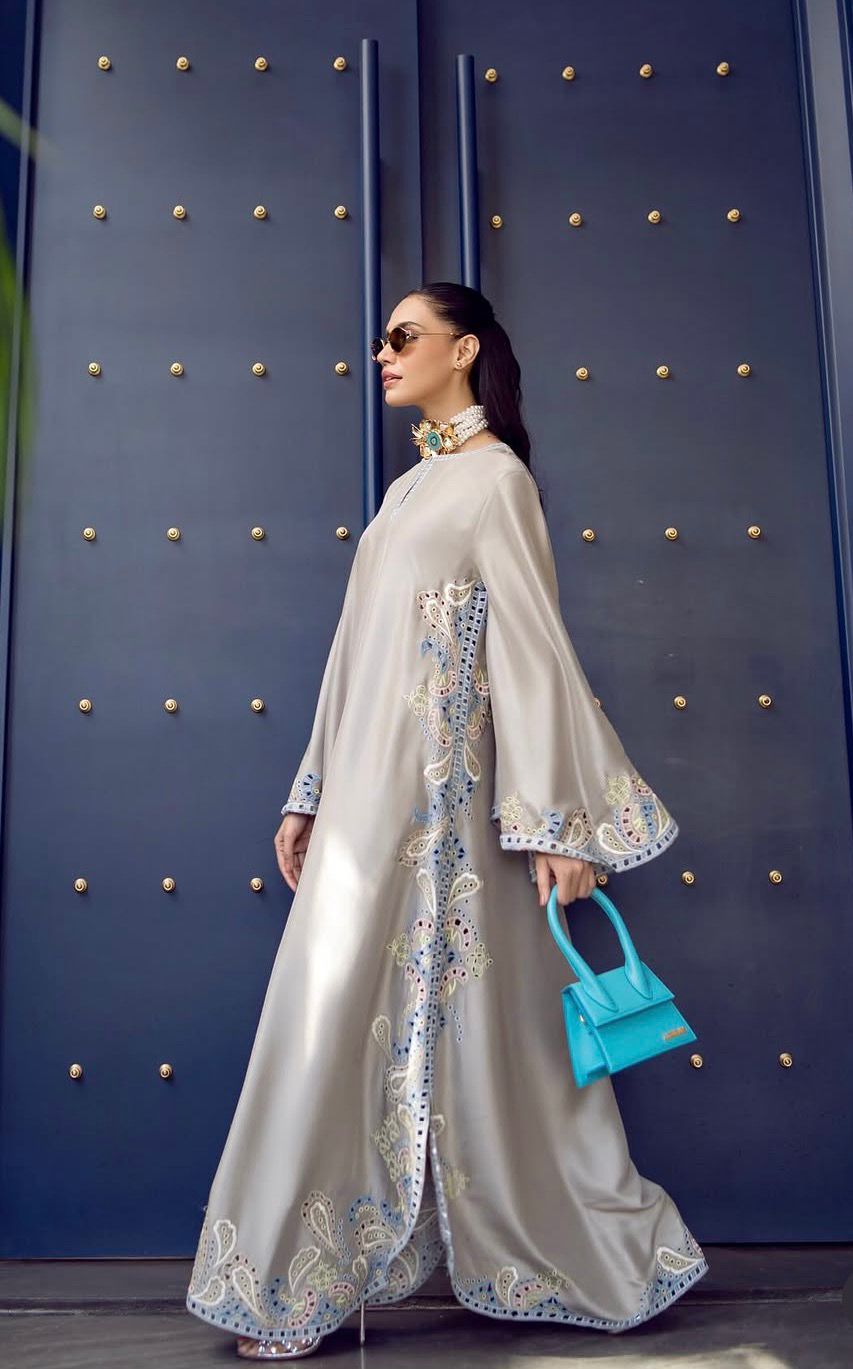 Woman in a white embroidered dress holding a blue handbag against a blue textured wall.