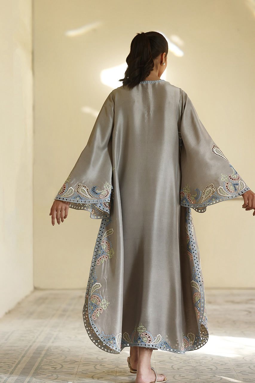 Woman wearing a long, light gray dress with intricate patterns in a softly lit room.